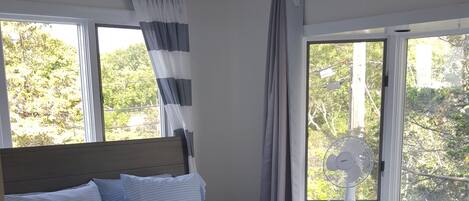 A bedroom with a bed, curtains, a window, and a fan.