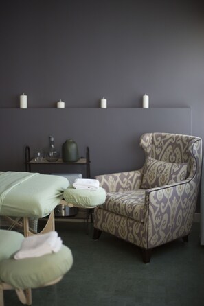 A room with a massage chair, a small table with candles, and a green bed.