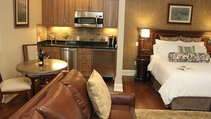 A compact hotel room with a kitchenette, a bed with patterned pillows, a brown leather sofa, and a small dining table with chairs. - Guesthouse at Norwalk Inn (Norwalk)