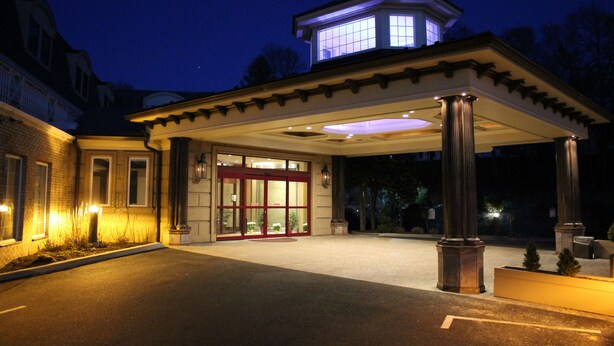 A hotel entrance with a covered walkway, a prominent tower, and a well-lit facade. - Guesthouse at Norwalk Inn (Norwalk)