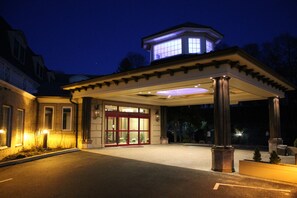 A hotel entrance with a covered walkway, a prominent tower, and a well-lit facade. - Guesthouse at Norwalk Inn (Norwalk)