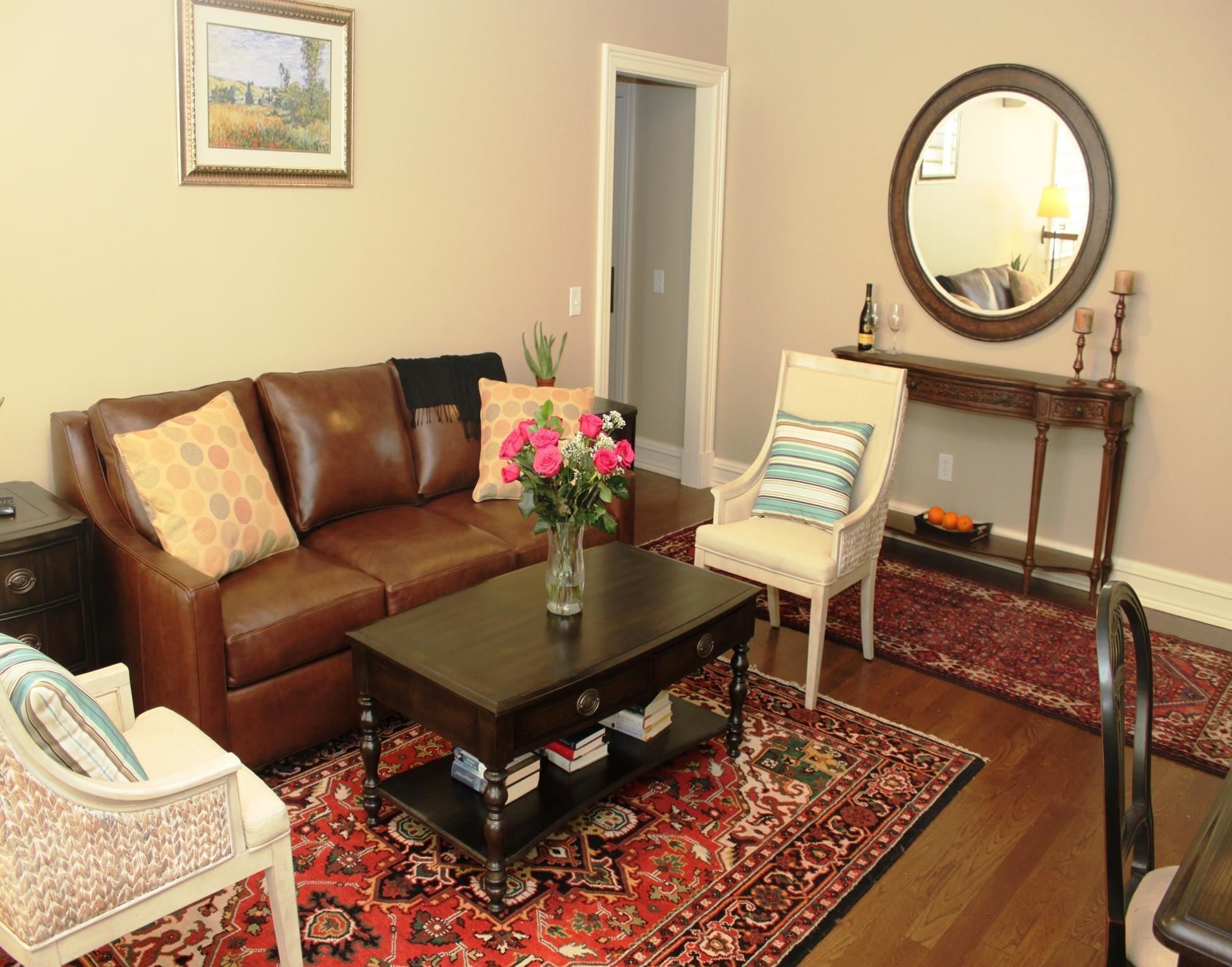 A living room with a brown leather sofa, a white armchair, a coffee table, and a patterned rug.