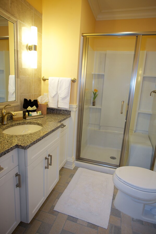 A bathroom with a sink, mirror, glass shower enclosure, and toilet. - Guesthouse at Norwalk Inn (Norwalk)
