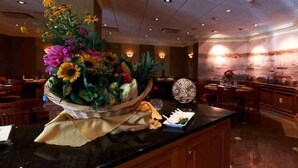 A restaurant interior with a large floral centerpiece on the counter, wooden furniture, and a wall with nautical-themed artwork. - Guesthouse at Norwalk Inn (Norwalk)