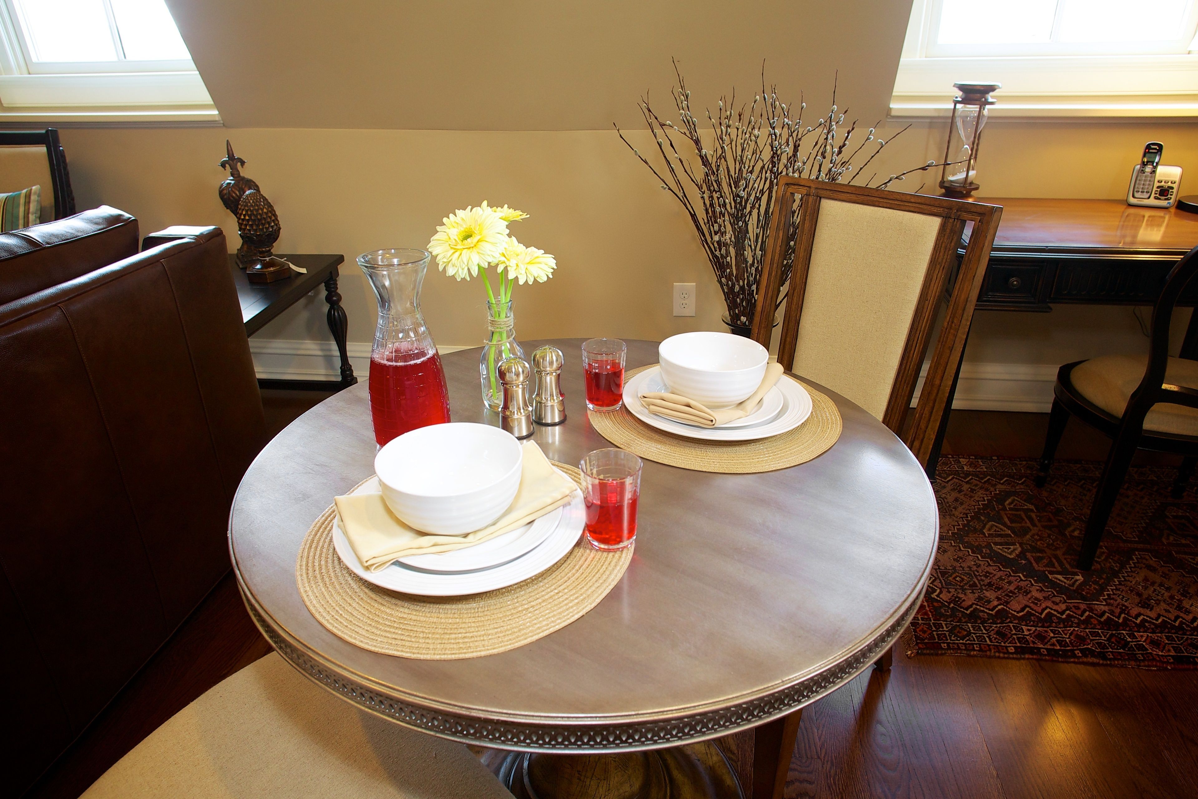 A dining table set with plates, bowls, napkins, and a vase with flowers.