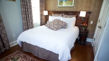 A neatly made bed with white linens and patterned pillows, a wooden headboard, and a small bedside table with a lamp.