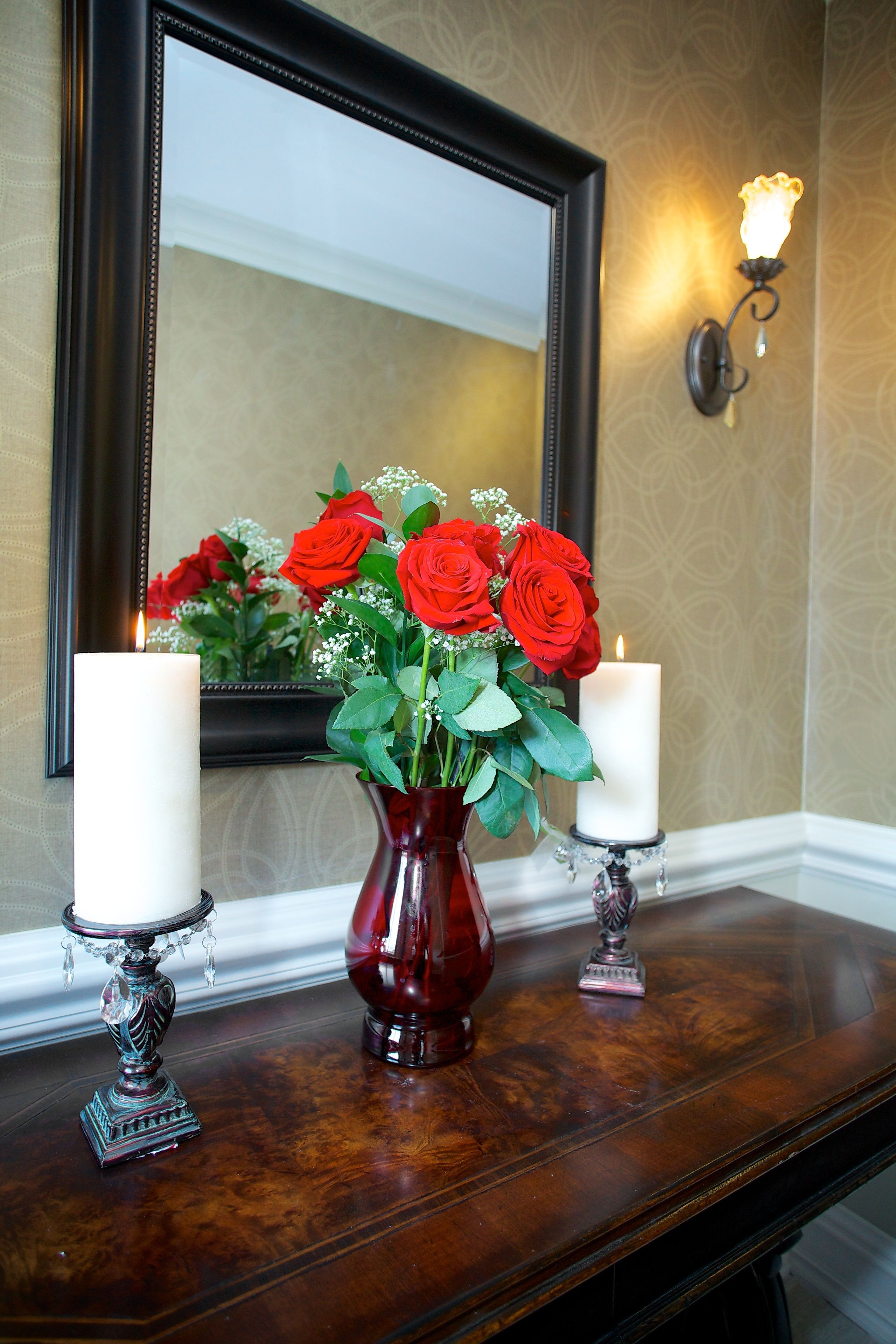 A wooden console table with a vase of red roses and two lit candles.