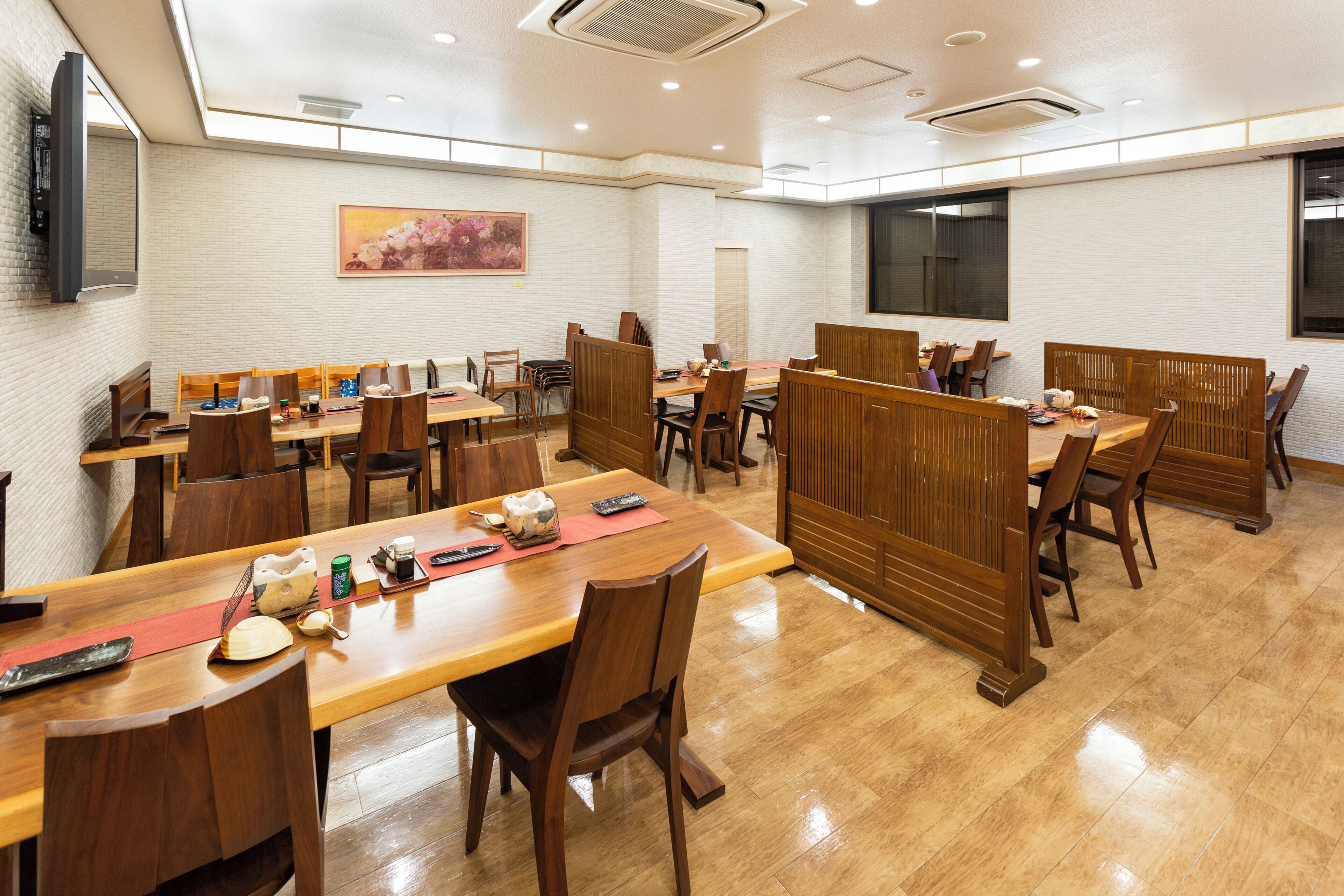 A restaurant with multiple wooden tables and chairs, a painting on the wall, and a large window.