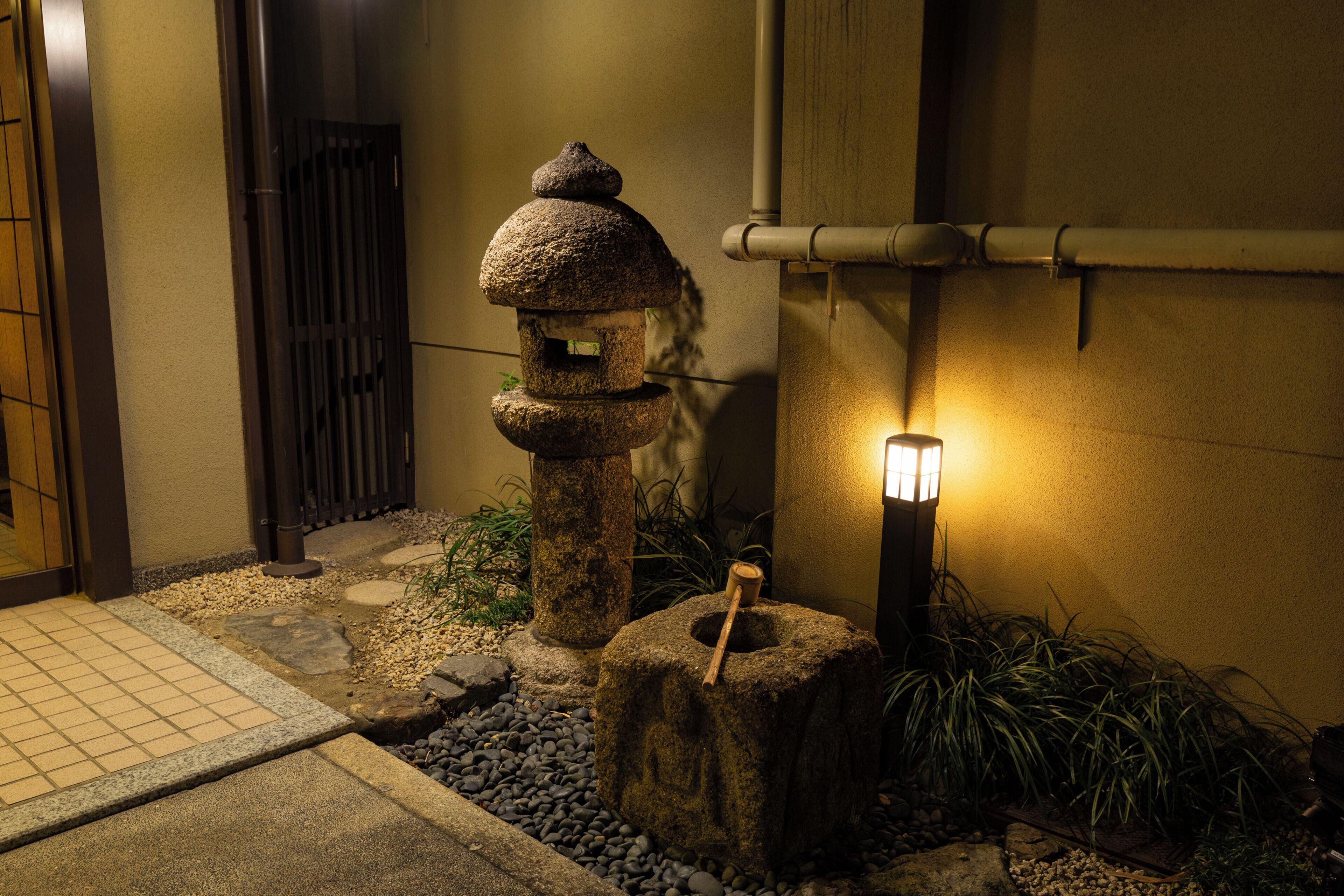 A traditional Japanese lantern in a garden setting with a pathway and a building entrance.
