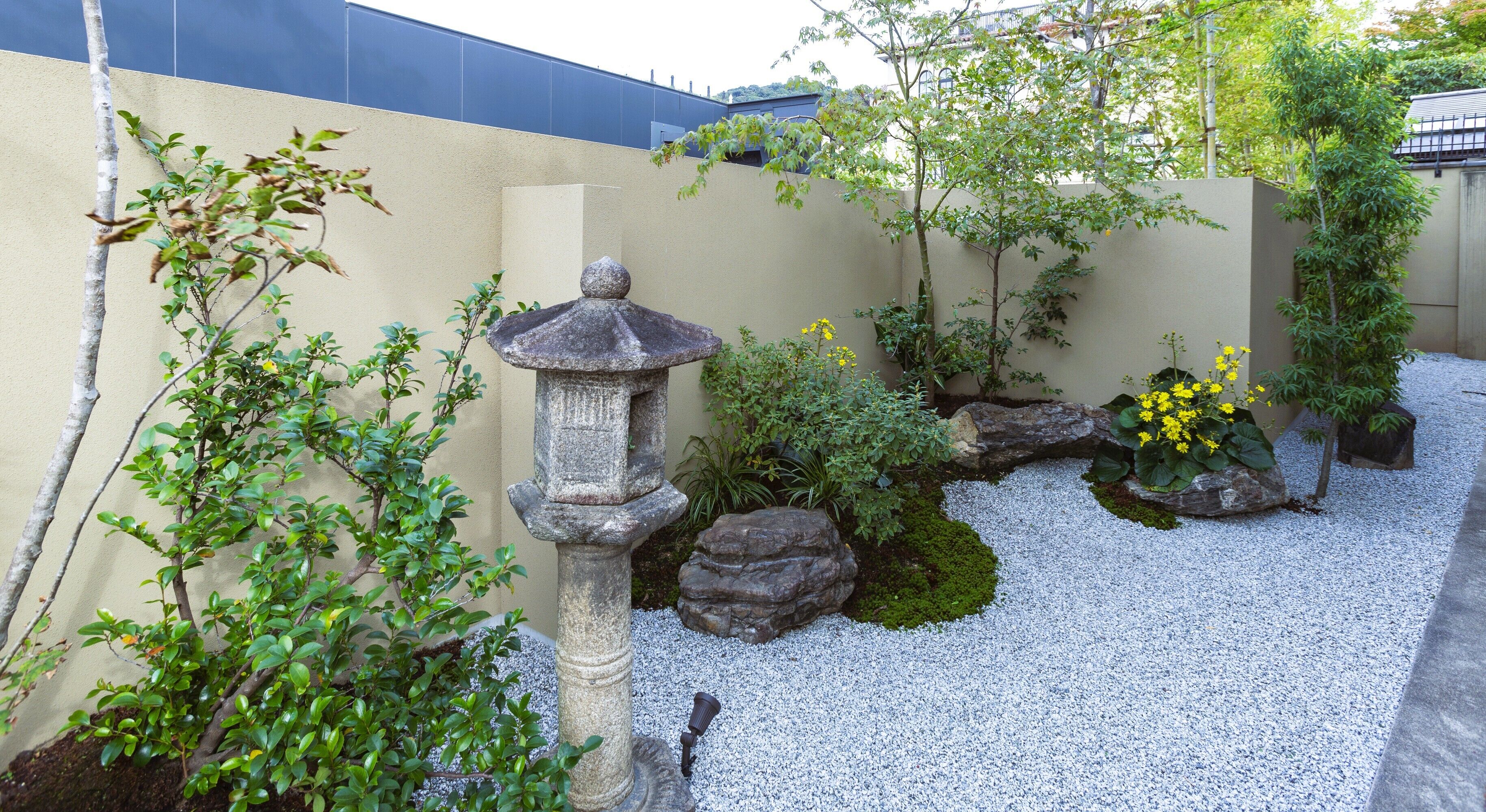 Un jardín con un farol de piedra, un sendero de grava y diversas plantas.