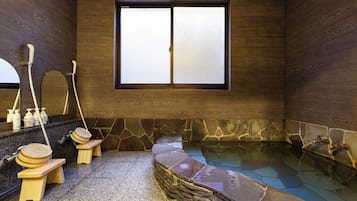 A traditional Japanese-style bathroom with a stone hot tub, wooden benches, and a large window.