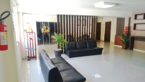 A spacious lobby with a black leather sofa, a potted plant, and a fire extinguisher on the left. - Sayuri Hotel (Foz do Iguaçu)