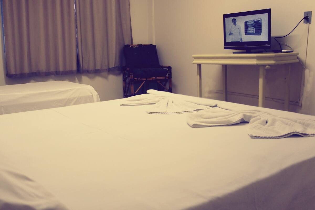 A hotel room with two beds, a television on a stand, and a chair.