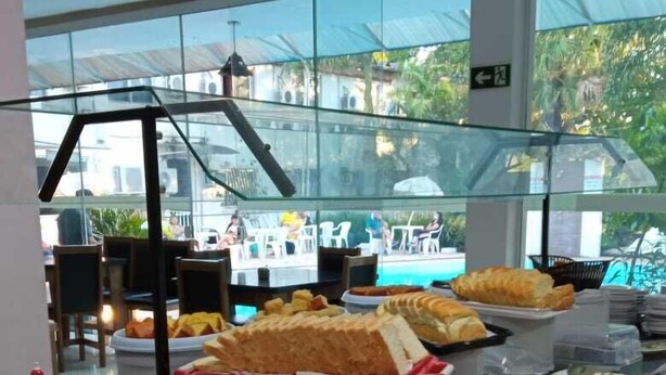 A buffet counter with various food items and a glass display case. - Sayuri Hotel (Foz do Iguaçu)