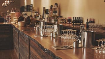 A bar area with wooden bar counters, hanging light fixtures, and a variety of bottles and glasses.