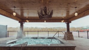 Un espace avec un bain à remous, doté d’un plafond en bois, de murs en pierre et offrant une vue sur les arbres en arrière-plan.