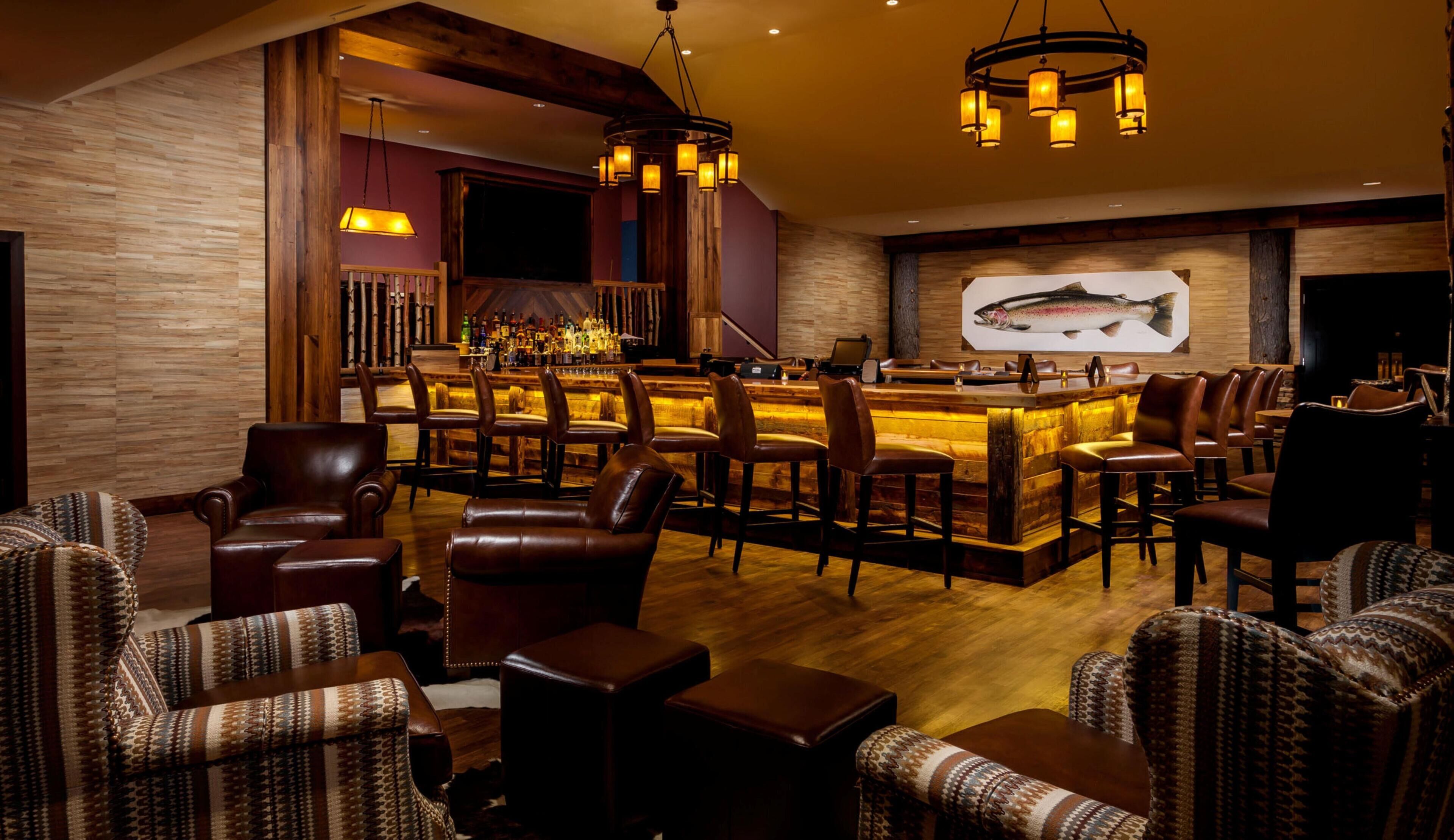 A bar area with leather chairs, a wooden bar counter, and a fish mural on the wall.