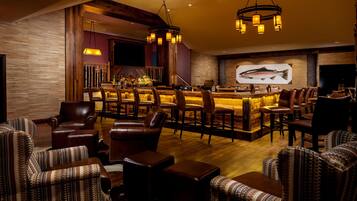 A bar area with leather chairs, a wooden bar counter, and a fish mural on the wall.