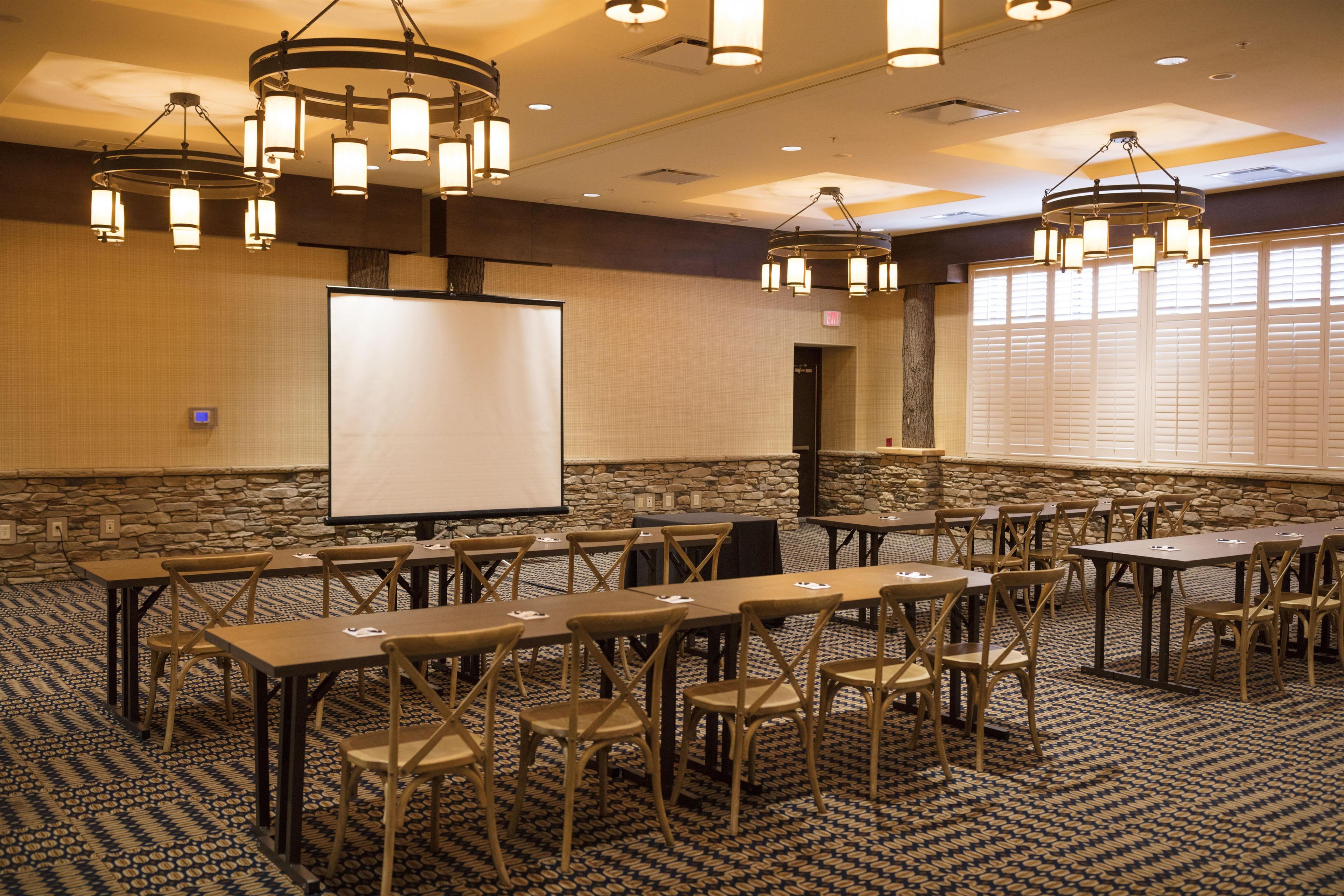 A conference room with a whiteboard, tables, chairs, and a stone wall.