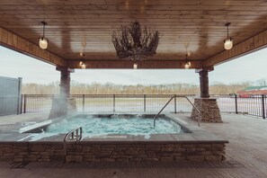 A covered outdoor hot tub area with stone walls and a metal railing.
