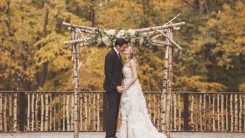 Una pareja se besa bajo un arco de madera adornado con flores blancas.
