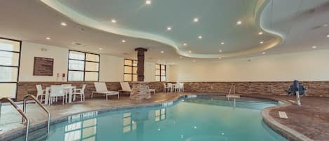 Une piscine intérieure à l’eau claire, entourée de chaises longues blanches et d’un pilier en pierre.