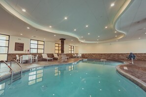An indoor swimming pool with clear water, surrounded by white lounge chairs and a stone pillar.