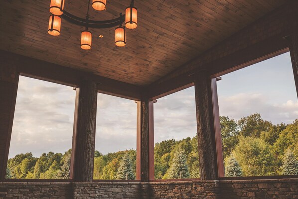 A room with a stone wall, large windows, and a wooden ceiling with hanging lights.