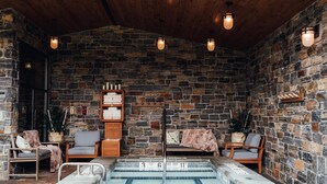 Une pièce aux murs de pierre, dotée d’une piscine, d’un plafond en bois et de plusieurs coins salon.