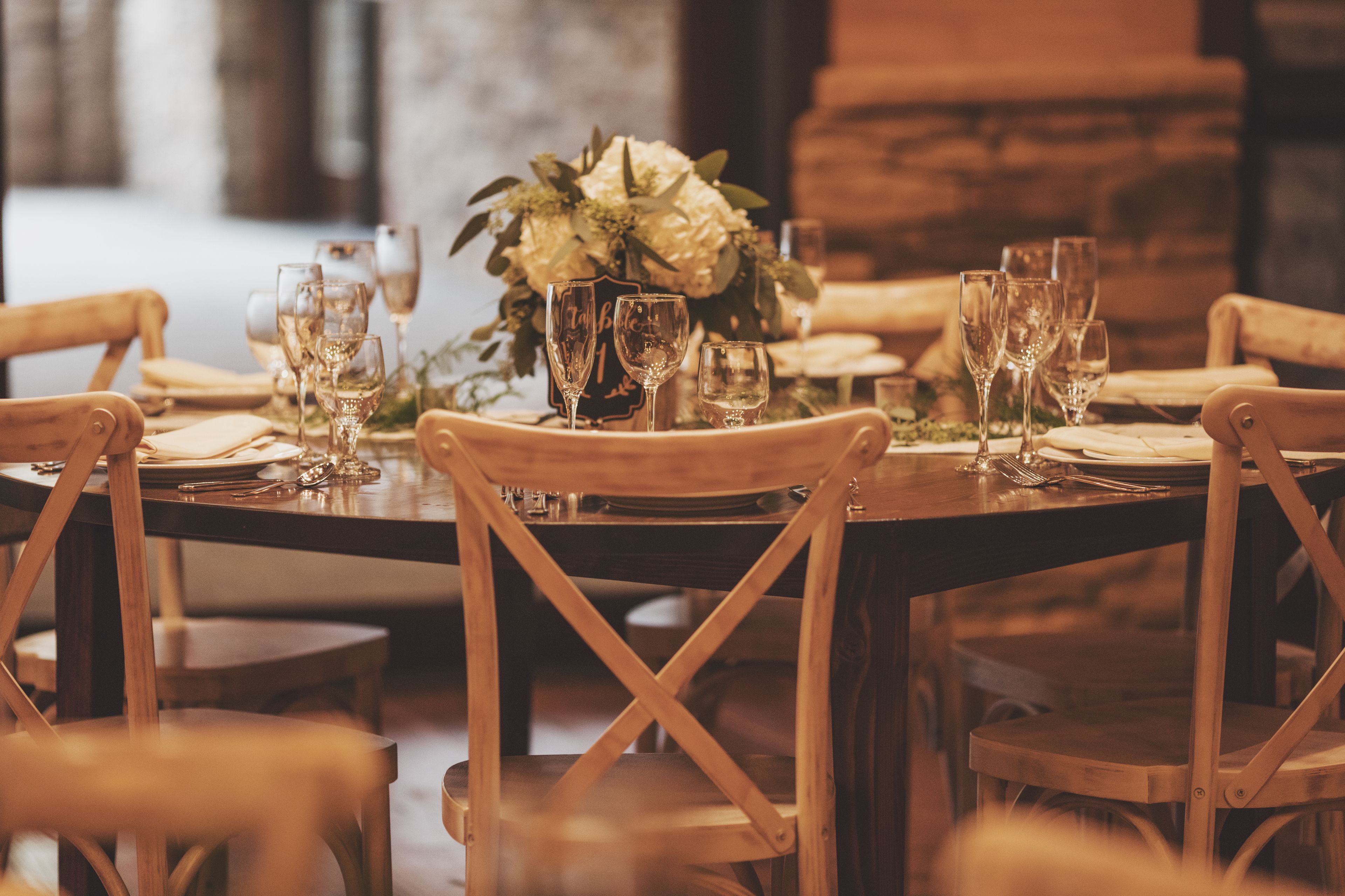 A dining table set with wine glasses, plates, and cutlery, surrounded by wooden chairs.