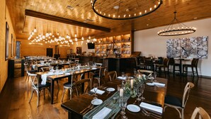 Un restaurant doté de plafonds en bois, de lustres et d’un bar. Les tables sont dressées avec des nappes blanches et décorées de bougies.