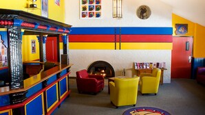 A brightly colored room with a fireplace, red and yellow chairs, and a wooden bar area.