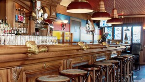 A bar area with wooden bar counters, multiple stools, and hanging pendant lights.