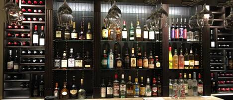 Uma área de bar com prateleiras cheias de garrafas de bebidas, copos e um balcão.