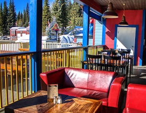 A red leather sofa and chairs on a wooden table with a menu, set against a blue and red wall with a view of a building and trees. - The Bulldog Hotel Silver Star (Silver Star Mountain)