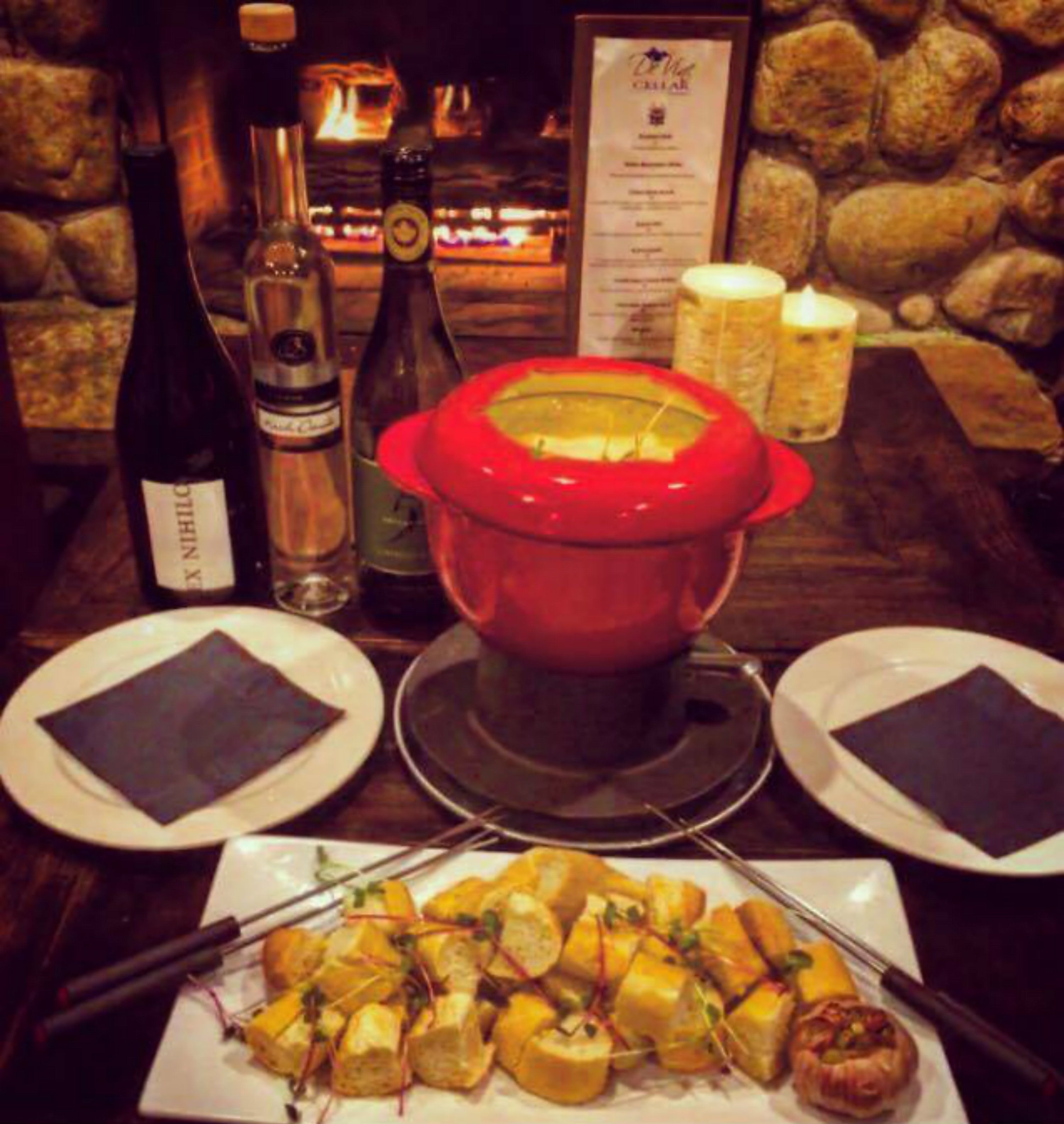 A dining table with a red pot, bottles of wine, and a menu.