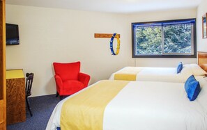 A hotel room with two beds, a red chair, a wooden shelf, a television, and a window with a view of trees.