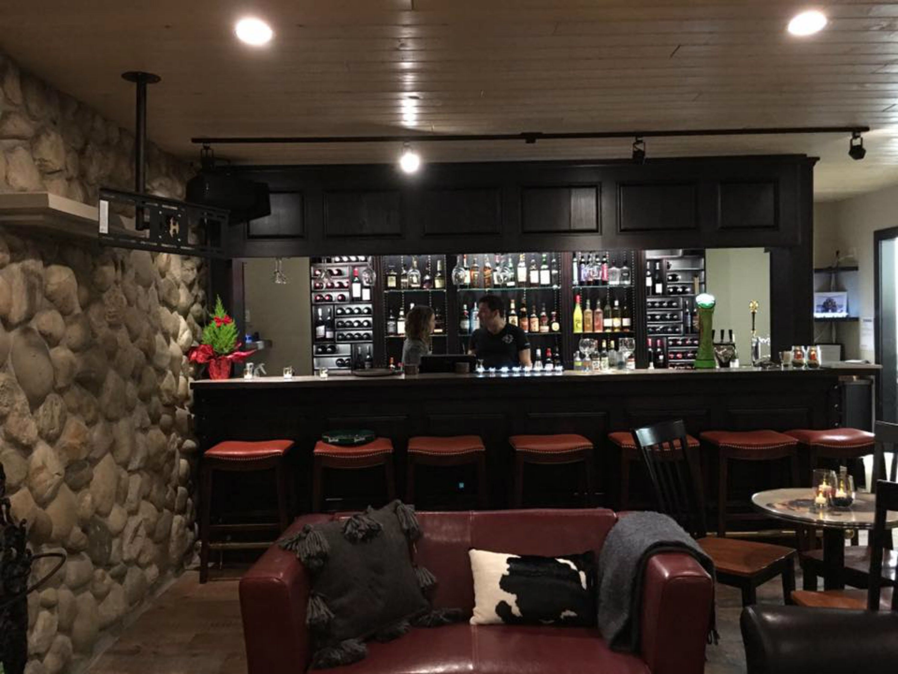 Un espace bar avec un mur en pierre, de nombreux tabourets, un comptoir et un barman.