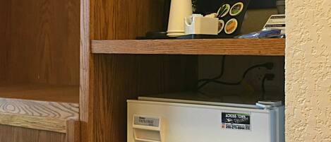 Une cuisine avec un réfrigérateur blanc, une machine à café et un porte-tasse sur une étagère en bois.