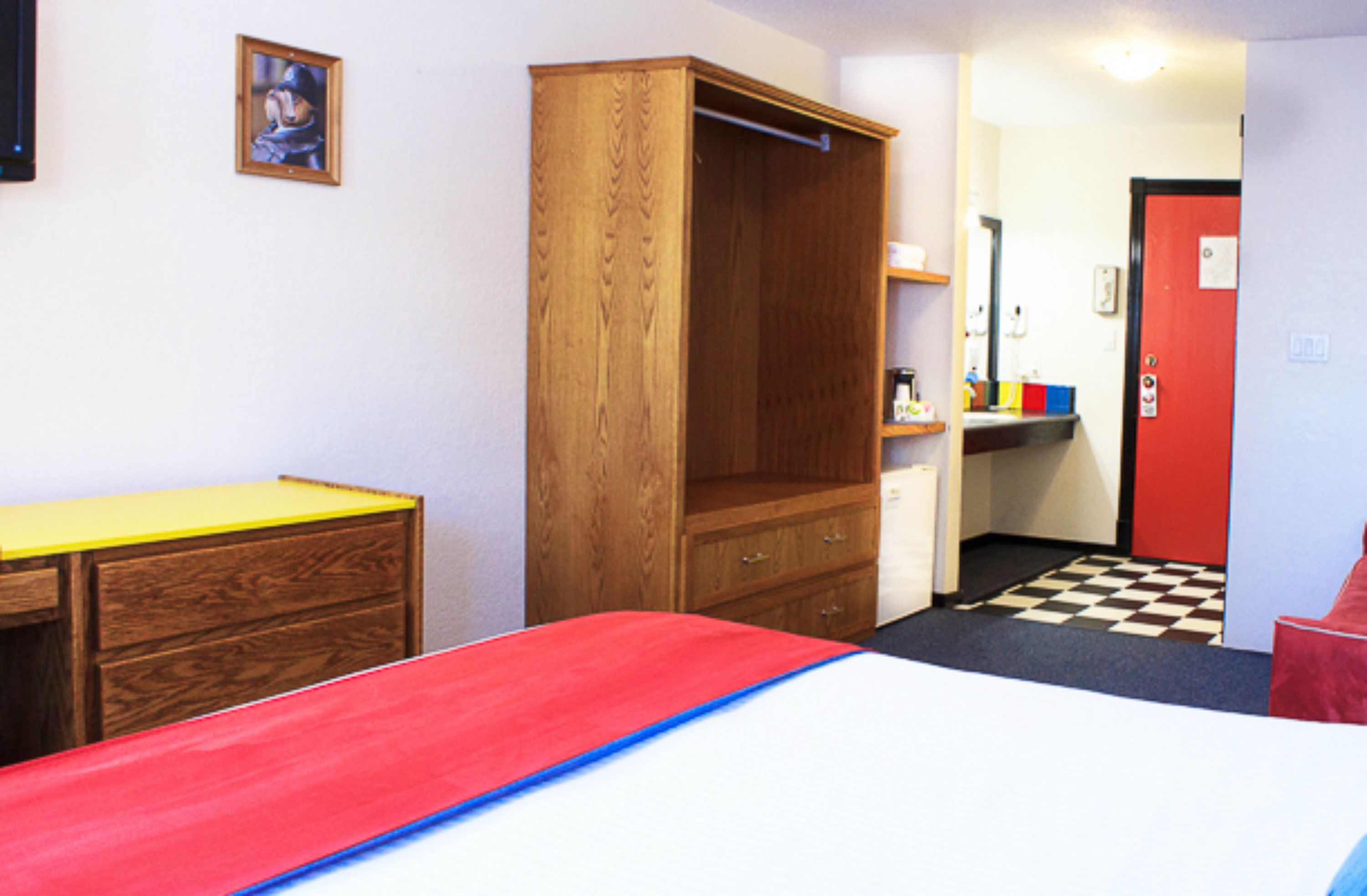 Een kamer met een bed, een houten garderobe, een bureau en een rode deur.