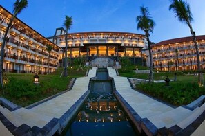 A multi-story hotel with a central courtyard, palm trees, and a water feature. - Lorin New Kuta Hotel (Pecatu)