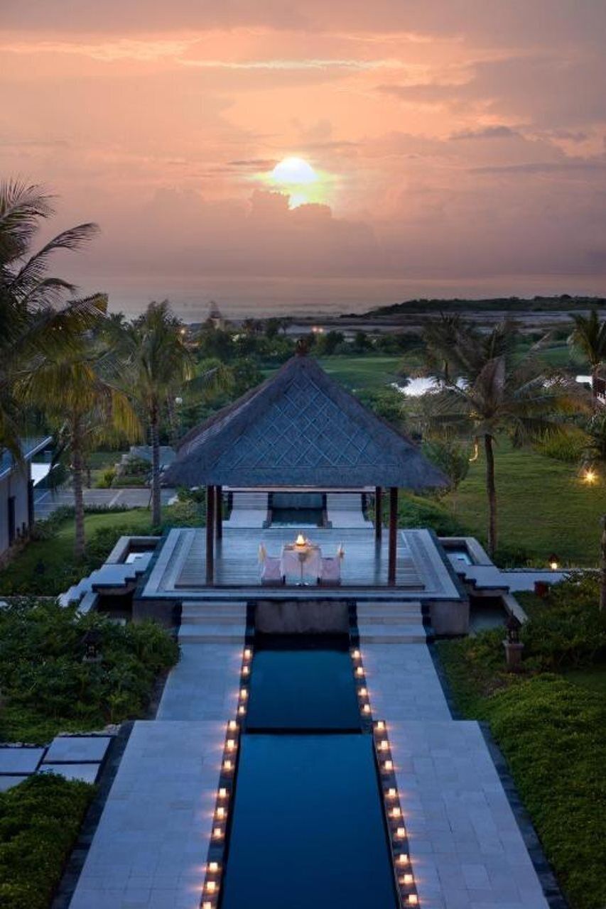 A pool area with a gazebo, surrounded by palm trees and a sunset view.