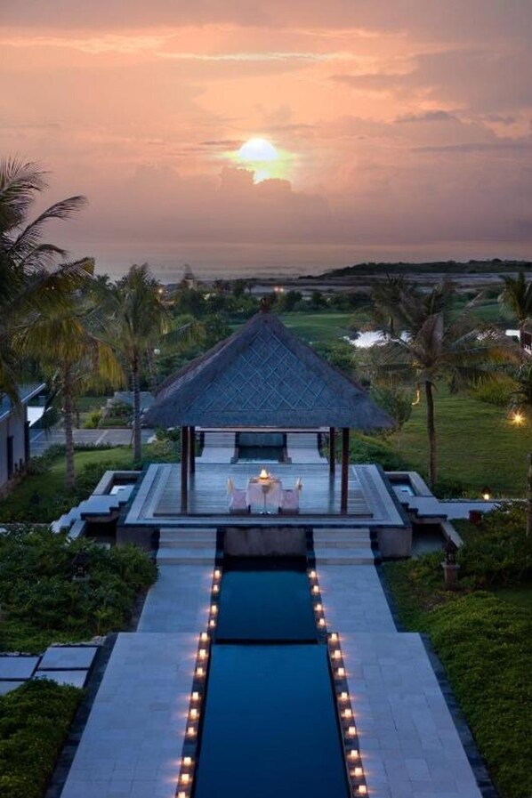 A pool area with a gazebo, surrounded by palm trees and a sunset view. - Lorin New Kuta Hotel (Pecatu)