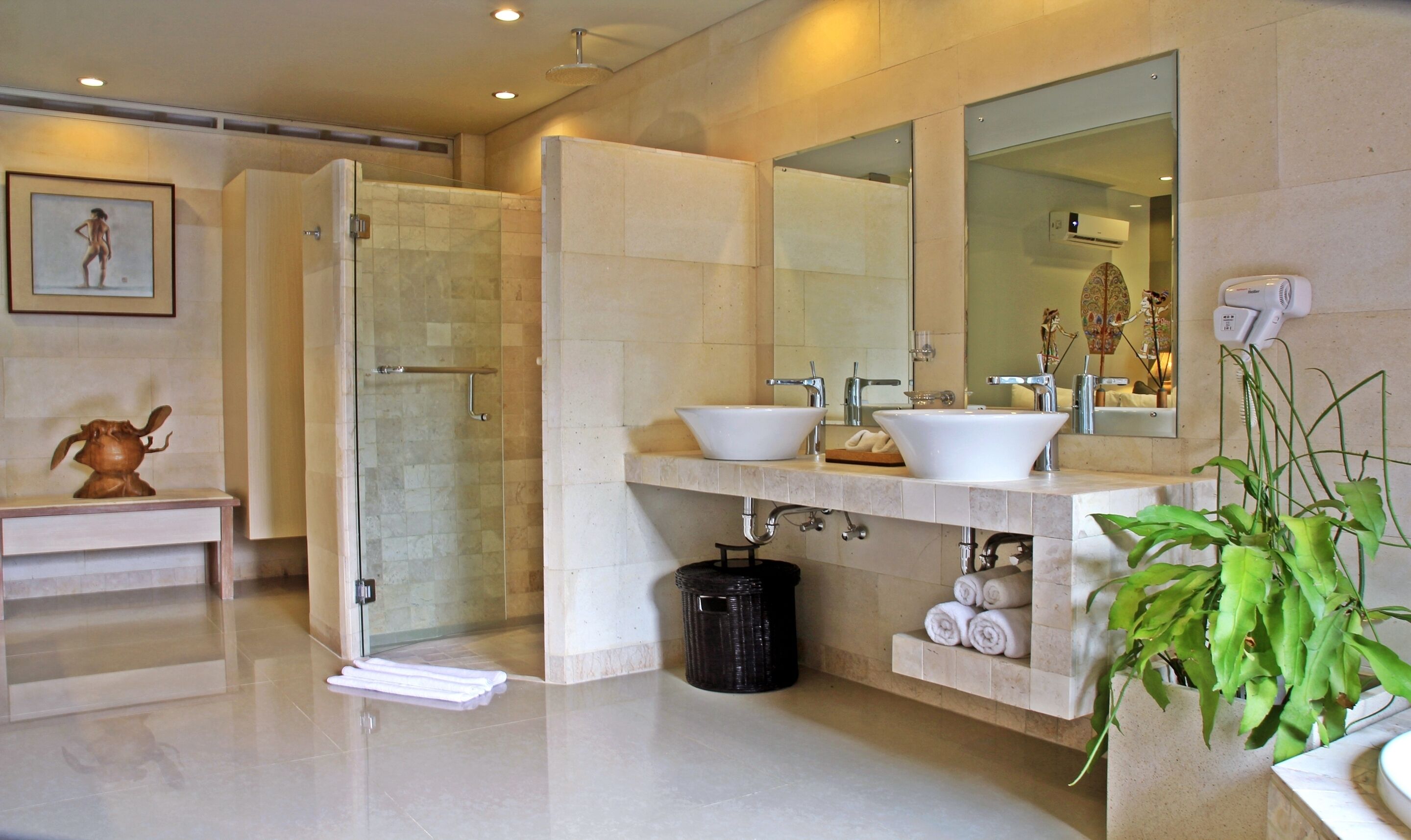 A modern bathroom with a glass-enclosed shower, two sinks, a large mirror, and a potted plant.