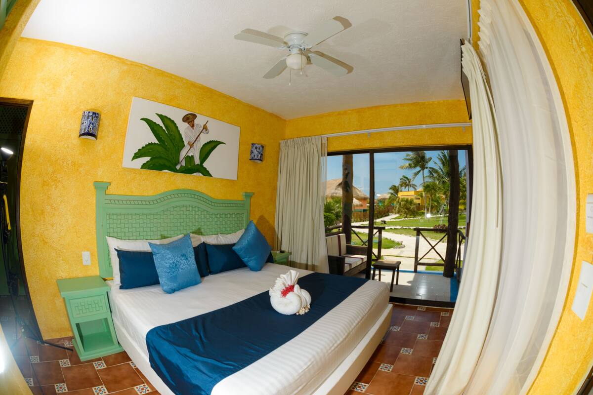 A hotel room with a bed, a ceiling fan, a window with curtains, and a view of the outdoors.