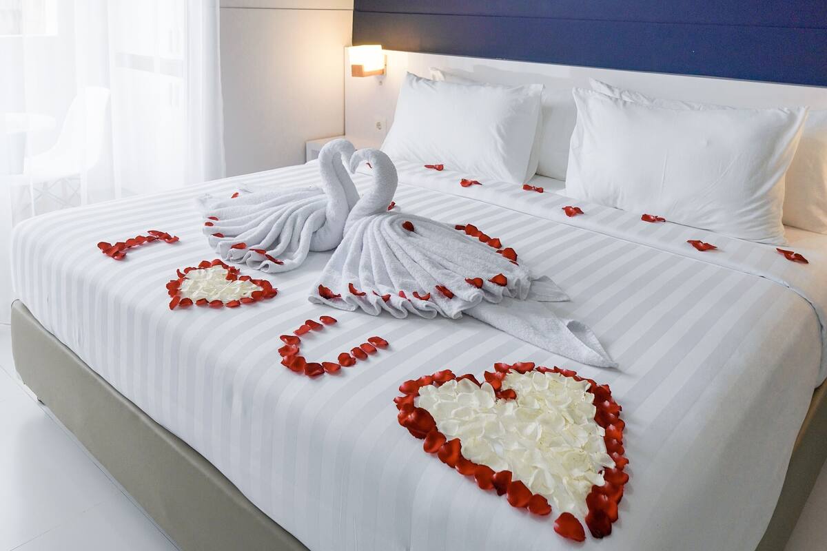 A neatly made bed with a swan towel and heart-shaped flower arrangements.