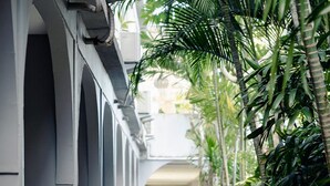 A corridor with a concrete floor, white walls, and a row of palm trees. - Cozy Stay (Denpasar)