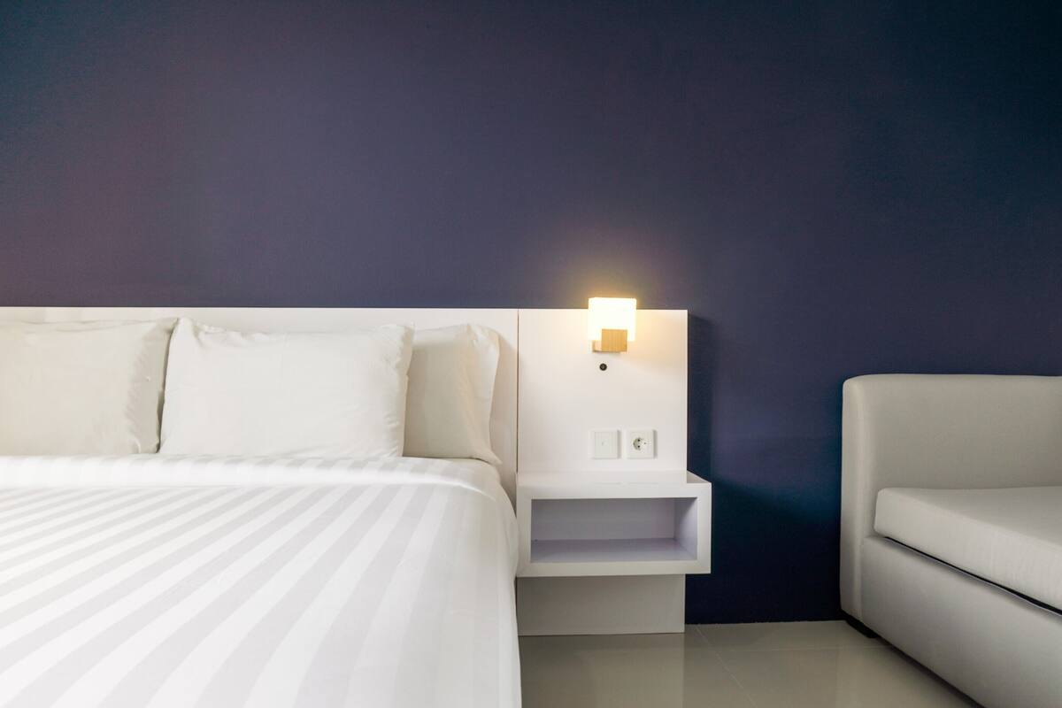 A neatly arranged hotel room with a bed, a nightstand, and a sofa.