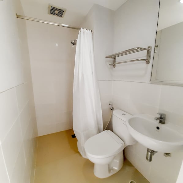 A small, clean bathroom with a toilet, sink, and shower area. - Cozy Stay (Denpasar)
