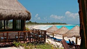 A beachside resort with thatched-roof huts, lounge chairs, and a wooden deck overlooking the ocean. - Hotel Sol Caribe (Punta Allen)